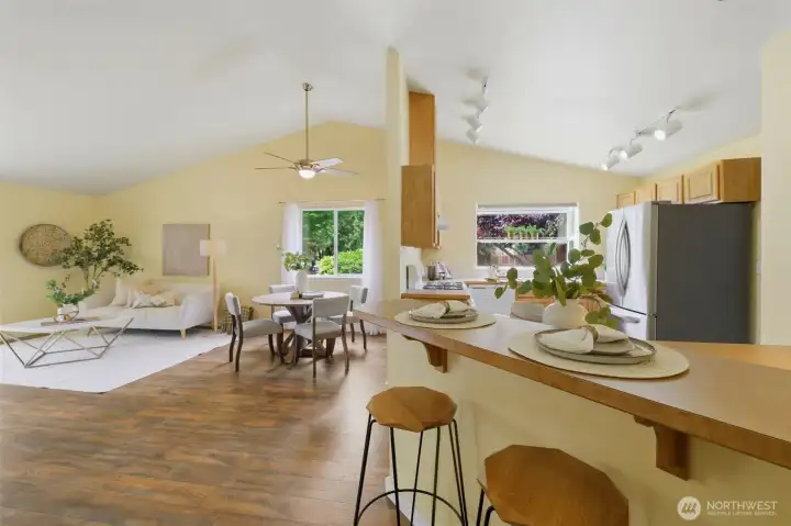 The open concept layout shines: vaulted ceilings, ceiling fan, dining area, and breakfast bar all connected by rich LVP flooring.
