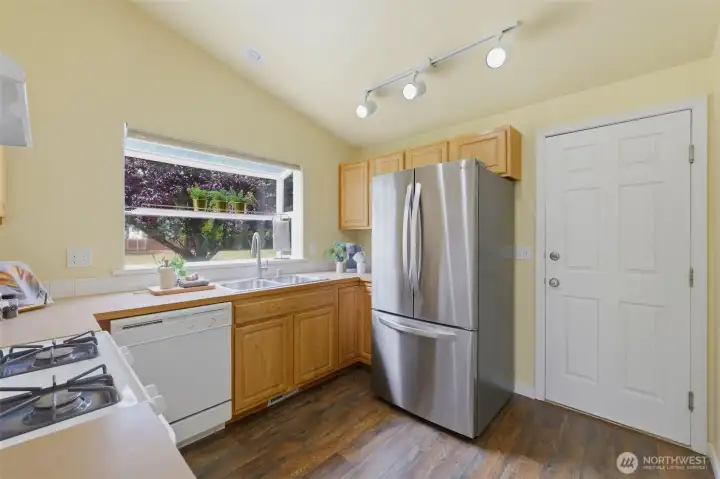 The kitchen offers a gas range, newer stainless steel refrigerator, and a charming garden window over the sink — bright and functional for the home chef.