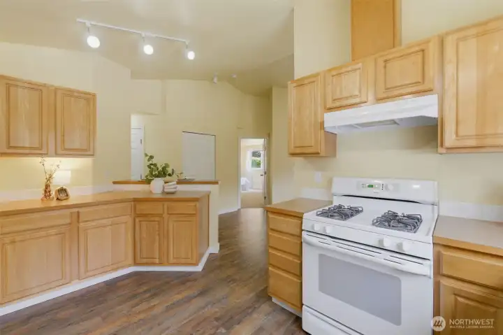 Warm wood cabinetry, gas cooking, and abundant counter space — plus a breakfast bar peninsula connecting the kitchen to the main living space.