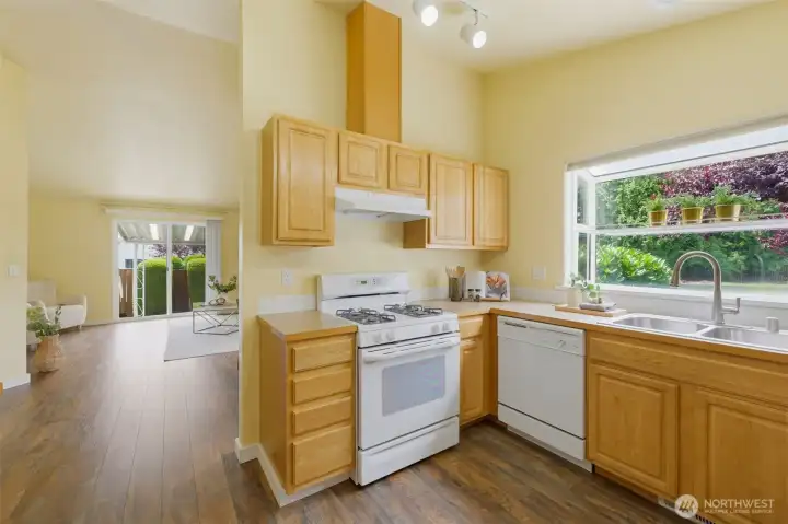 Efficient U-shaped kitchen with gas range, garden window over the sink, and durable Luxury Vinyl Plank flooring flowing into the open living areas.