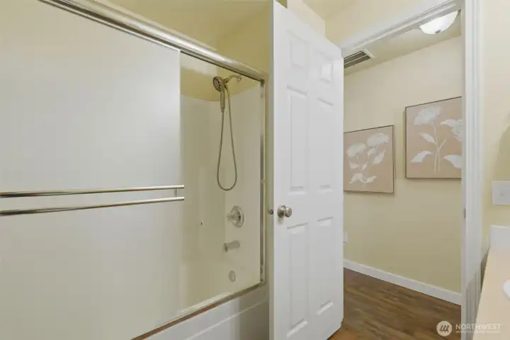 Tub and shower combo with glass sliding doors and handheld showerhead.