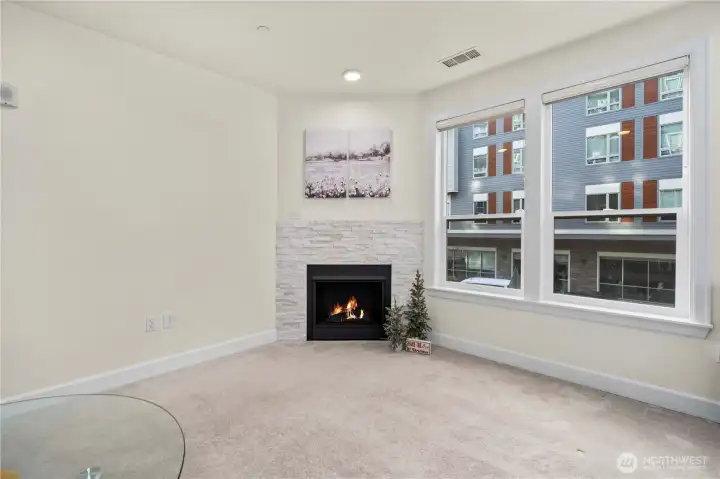 This perspective showcases the room’s oversized windows, which fill the space with daylight. The elegant fireplace adds warmth and modern style, enhancing the comfortable feel of the main living area.
