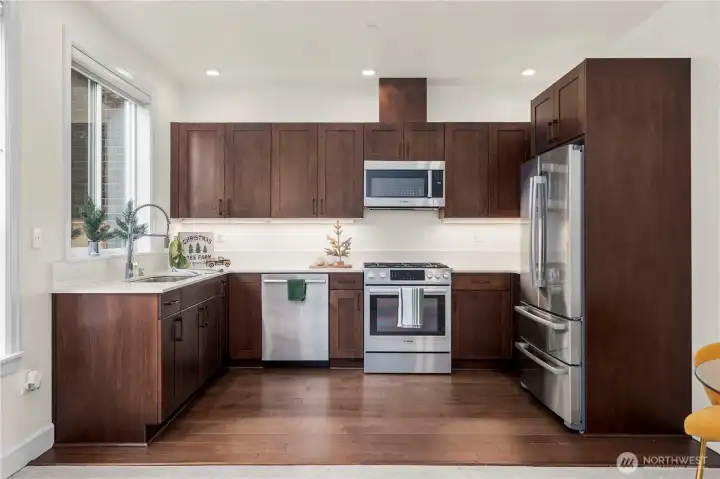 A spacious kitchen featuring rich wood cabinetry, sleek quartz counters, and premium stainless steel appliances. The clean design and ample storage make meal prep effortless while maintaining a modern, streamlined look.