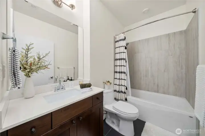 The main hallway bath features a clean, modern design with a full tub and tile-surround shower. A spacious vanity with quartz counters and rich wood cabinetry provides ample storage, while soft neutral tones create a welcoming, refreshed atmosphere.