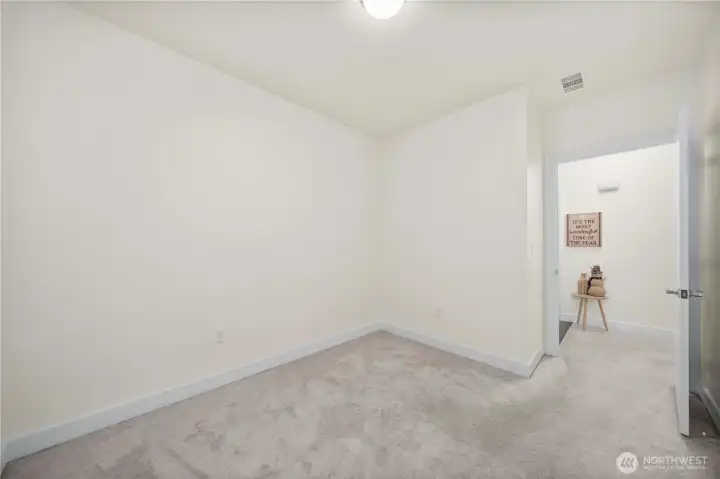 Another view of Secondary Bedroom showcases its open floor area and convenient hallway access. This flexible space adapts to your lifestyle needs and offers a peaceful retreat within the home’s efficient layout.