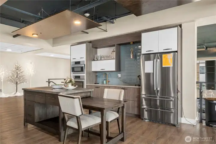 The stylish community kitchen features contemporary cabinetry, a large island, and stainless steel appliances—ideal for entertaining, potlucks, or shared meals. Ample counter space and comfortable seating make it a functional and welcoming amenity.