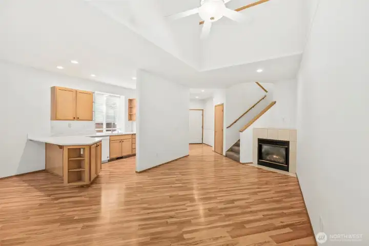 From window corner of living room looking out toward kitchen, gas fireplace, staircase, and entryway. Laminate hardwood flooring throughout main floor.