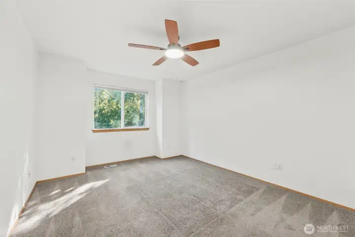 Primary bedroom with wall-to-wall carpet, ceiling fan, and en-suite bath, with window looking out towards the greenbelt and backyard.