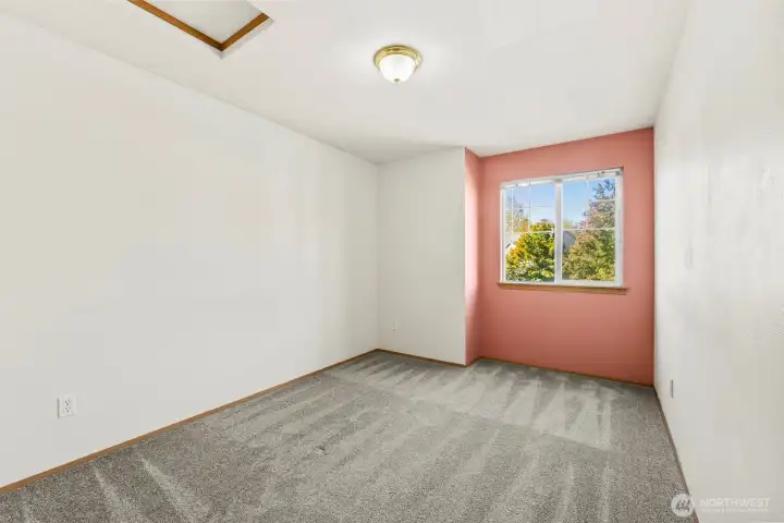 Bedroom 2 with wall-to-wall carpet, window looking out toward frontyard/street. Attic access point in ceiling.