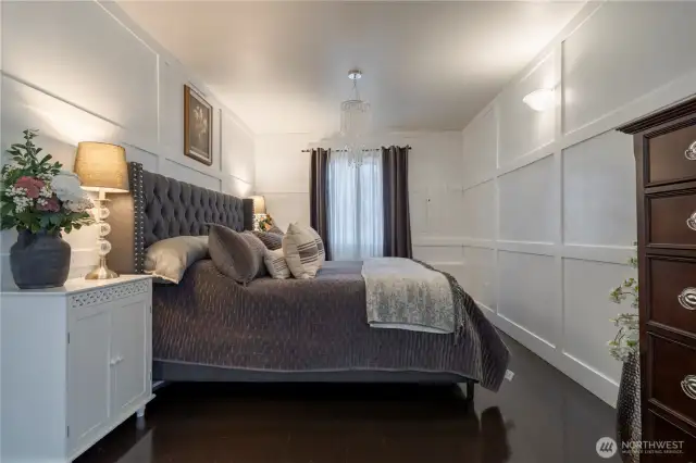 This main-level primary bedroom offers timeless elegance with coffered walls, hardwood floors, and a spacious layout