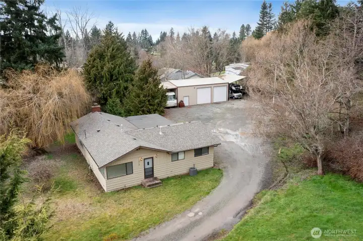 Aerial view showcasing the home, expansive gravel drive, and large detached shop—perfect for projects, storage, or future creative use.