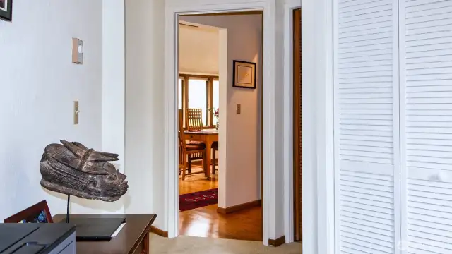 Looking from side room in primary through hallway with half bath to DR. Door to primary full bath with laundry to far right of middle.