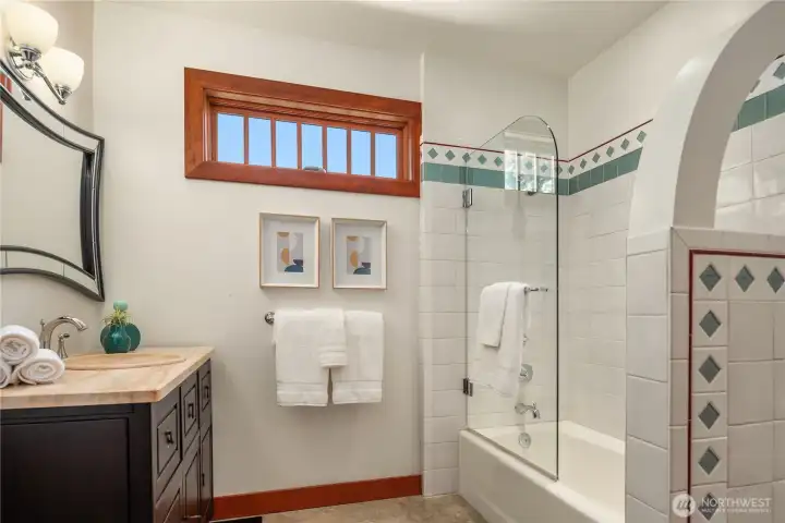 Charming main level (full) bathroom blends classic tile work and soaking tub with glass enclosure and a stylish vanity.