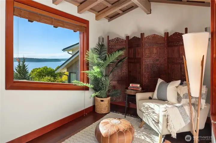A cozy reading nook framed by rich wood accents and expansive windows offers serene views of the Sound, creating a peaceful retreat on the upper level.