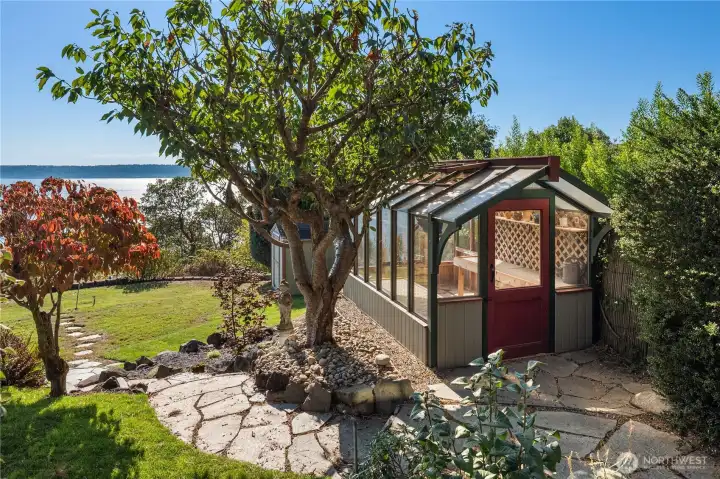 Charming greenhouse, nestled among mature trees and stone pathways, offers the perfect spot for gardening year-round while taking in the view.