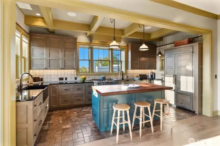 The kitchen is both warm and refined, featuring rich soapstone countertops, exposed beamed ceilings, and thoughtfully placed recessed lighting. Large windows frame water views in two directions, filling the space with natural light and creating a stunning, ever-changing backdrop.