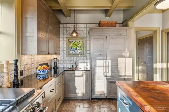 Throughout the home, you’ll notice thoughtfully crafted cased openings and distinctive leaded glass windows that add character and charm. In the kitchen, one such window sits above a beautifully hammered copper sink, creating a convenient secondary prep area that’s as functional as it is visually striking.