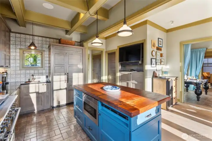From this angle, the kitchen opens gracefully toward the entryway and dining room beyond, highlighting the home’s seamless flow and inviting layout. Just beside the TV, you’ll find the door to a spacious walk-in pantry—perfectly suited for storing everything from everyday essentials to bulk purchases from Costco