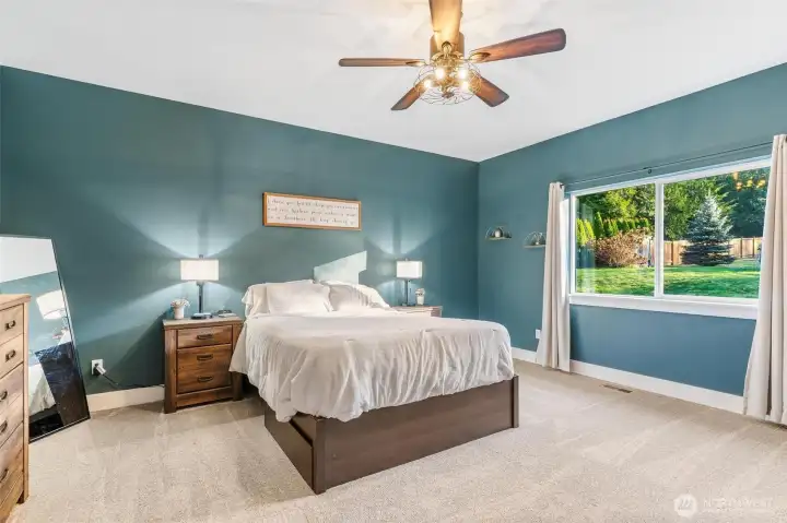 Open, spacious primary bedroom with large window and ceiling fan