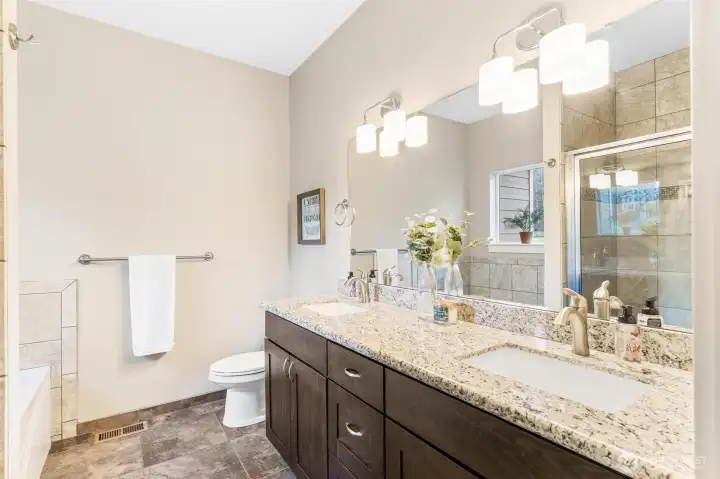 Dual sinks, stone countertops, bright lights in primary bathroom