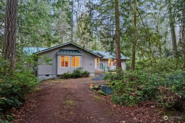 Exterior view features two bay windows and metal roof, deck on left side w/stairs to laundry room.