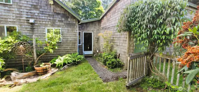 A picture-perfect entrance to this Nahcotta charmer—this garden path leads through lush greenery and thoughtfully placed plantings to a welcoming shingled doorway. Nestled among ferns and framed by climbing vines, it’s a whimsical blend of artistry and nature that sets the tone for the serene, storybook home beyond.