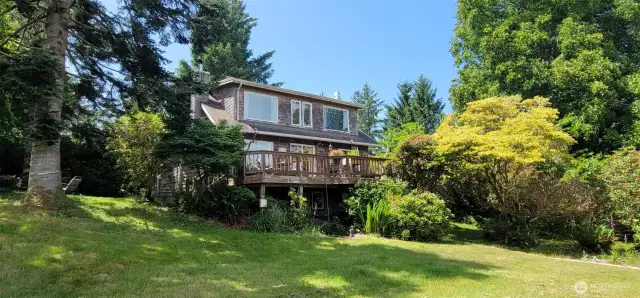 Bask in coastal serenity on this sun-drenched deck—framed by soaring evergreens and vibrant gardens, the open-air living space seamlessly extends from the home’s glass-lined façade, offering the perfect perch to enjoy tranquil Nahcotta evenings.