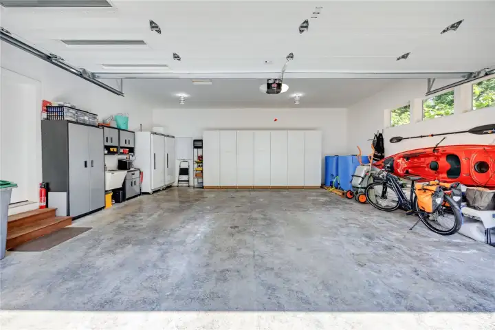 This immaculate oversized garage features a sleek, modern single-panel door and conveys with a commercial-grade fridge and freezer, built-in storage cabinets, and two 320-gallon emergency water tanks.
