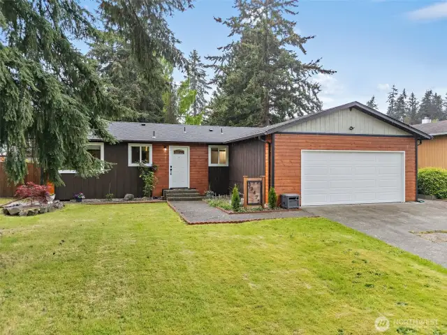 Another angle of the front exterior, showcasing the wide driveway, manicured lawn, and mature trees that add character and shade.