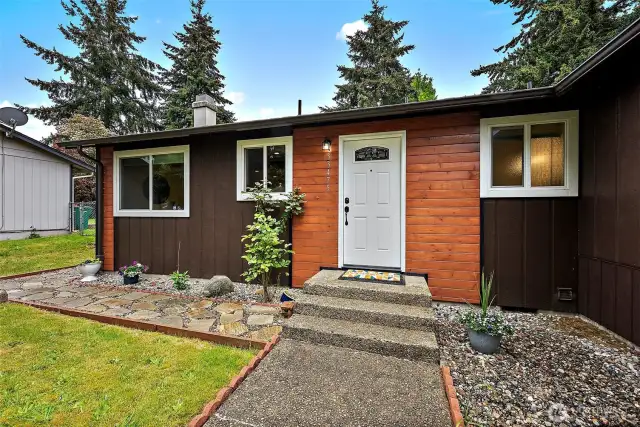 Step up to the front door and take in the charming blend of rich wood tones and fresh greenery—this cozy entrance sets the stage for what continues inside.