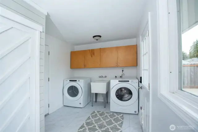 Cheerful laundry/mudroom - pantry in foreground, brand new luxe vinyl tile floors, access to garage at left and to back yard at right.