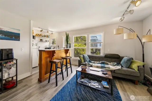 Apartment 3 – Natural Light Meets Timeless Craft  Sunlight pours through corner windows in this ground-floor one-bedroom, highlighting original Douglas fir floors and a crisp white brick fireplace. The open layout connects seamlessly to a warm kitchen with a built-in bar, offering space for both quiet evenings and casual entertaining. This unit’s blend of comfort and history makes it one of Laurel Gate’s most beloved.