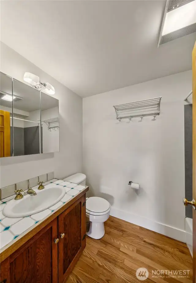 Apartment 7 Bath – Fresh, Functional, and Bright  Apartment 7’s full bath combines utility with warmth—featuring updated fixtures, a large vanity with storage, and hardwood floors that carry through from the main living space. A skylight above adds natural light, completing this clean and comfortable retreat within one of Laurel Gate’s most distinctive homes.