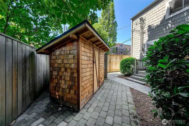 Landlord's Garden Shed – Discreet Utility, Tucked Beneath the Trees  Nestled off the brick-paved side path, this custom-built cedar shed provides secure, dry storage for landlord tools and seasonal supplies. Its compact footprint and craftsman styling blend seamlessly with the building’s character, supporting ease of maintenance while preserving the property’s tidy, park-like grounds.