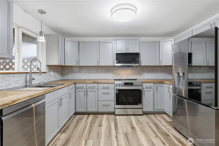 Stylishly remodeled kitchen with butcher block countertops, mosaic tile backsplash, new cabinetry, stainless steel appliances, and luxury plank vinyl flooring for a seamless transition from the living room.