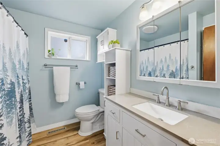 Bright and refreshed full bathroom with updated lighting, new sink and countertop, and a crisp, modern feel.