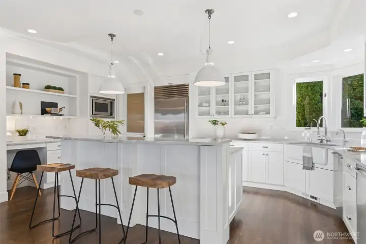 The kitchen in an inspiring and cheerful hub with solid wood, white painted shaker cabinetry, center island, and oversized enamel pendants from Schoolhouse Electric.