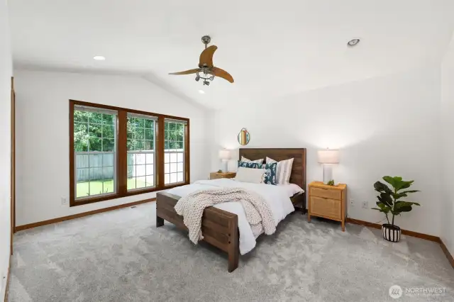 Retreat to your tranquil primary suite featuring vaulted ceilings, plush carpeting, and oversized windows that flood the space with natural light and offer peaceful views of the private backyard.