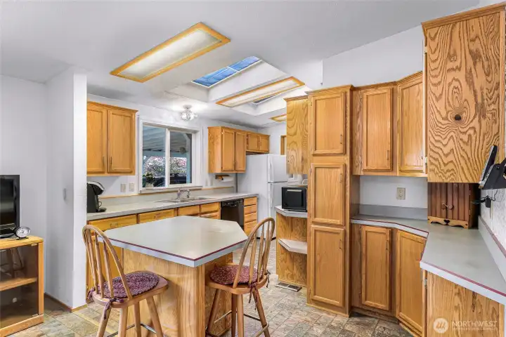 Spacious kitchen with skylights, breakfast bar, abundant cabinet storage, and open flow to dining area and deck access