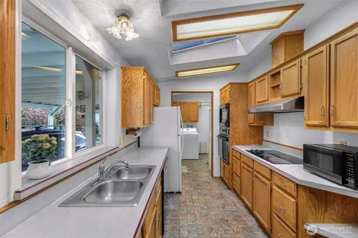 Light-filled kitchen featuring skylights, extensive cabinetry, generous prep space and adjoining utility area