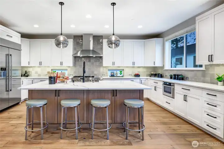 Showstopping chef’s kitchen featuring an oversized island, JennAir appliances, luxe tile backsplash, quartz counters, and abundant cabinetry storage.