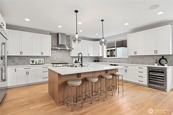 Showstopping chef’s kitchen featuring an oversized island, JennAir appliances, luxe tile backsplash, quartz counters, and abundant cabinetry storage.