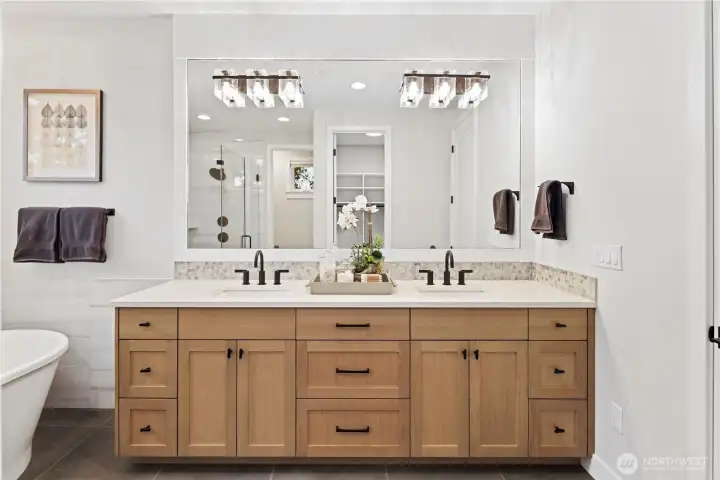 The primary bath features a large double vanity with rich wood cabinetry, quartz countertops, and a full-width mirror illuminated by modern crystal-accent lighting.