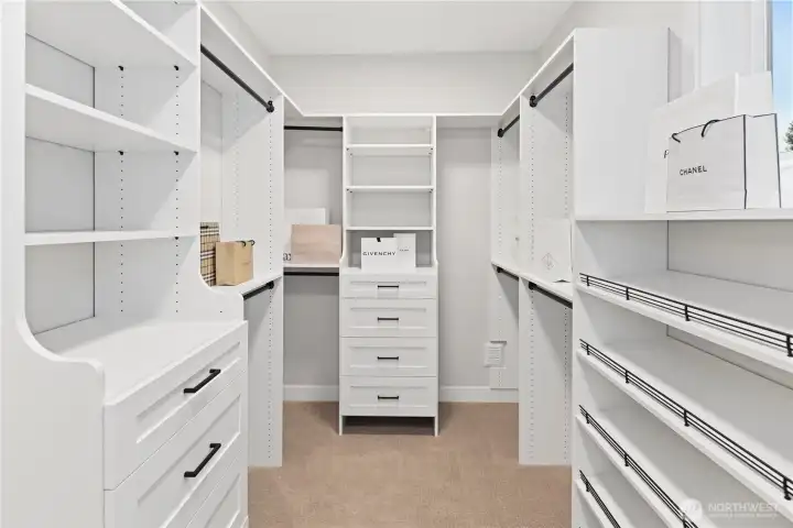 Spacious primary suite walk-in closet with custom built-ins, generous hanging space and shelving, shoe shelves, two banks of drawers, and a window brings in natural light.