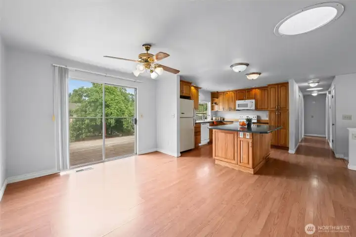 Open-concept dining with ceiling fan, sliding glass door to the deck, island kitchen, and same flooring throughout the upstairs, making spaces feel expansive. The layout is already doing the work. Swap the finishes and this space transforms completely. The bones buyers are hunting for.