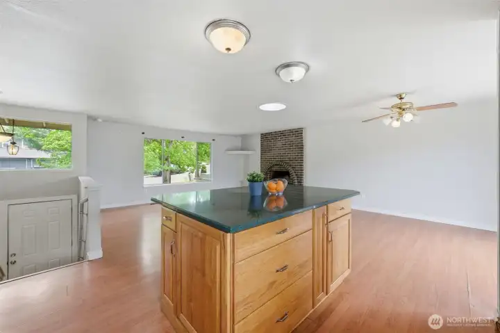 Kitchen island with granite top and deep drawers, open flow to the living room, brick fireplace anchoring the living room. Add some pendant lighting as the wiring is in place! The layout is the asset.