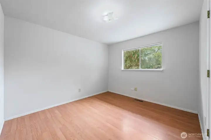 Bedroom Two features a serene tree-framed window view, warm laminate flooring, and enough square footage to grow into — whether that's a guest room, nursery, or the home office you've been dreaming about.