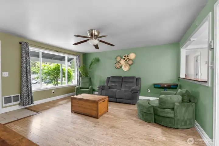 :iving room features plank style flooring,arge white vinyl windows, open space between kitchen and living area and remote control fan