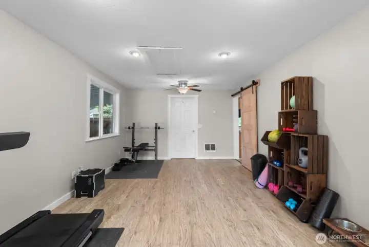 Huge flex space with barn door slider to Kitchen, wood grain laminate flooring, large bright white vinyl windows, access to Utility room.