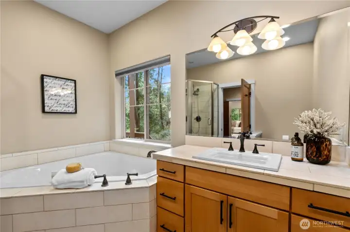 Soaking tub with tile surround positioned beside a large window with wooded views